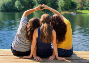 Image of three friends doing a heart shape with their hands over the friend in the middle.