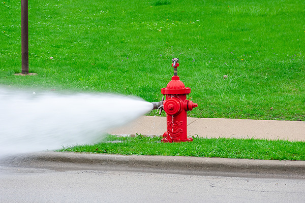 Red fire hydrant being flushed, high pressure water spraying.